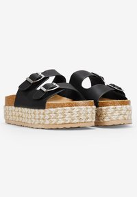 Sandales à plateforme noires avec deux brides réglables et des boucles en argent, dotées d'une semelle intermédiaire en jute tissé et d'une semelle en liège pour un confort optimal.