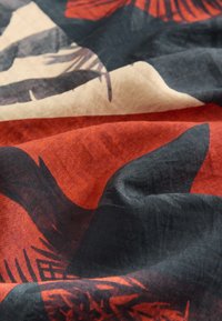 Tessuto con un motivo astratto rosso e nero, caratterizzato da una trama morbida e liscia e da evidenti disegni di foglie di palma nere su uno sfondo beige.