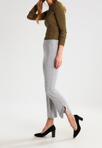 Brun och gulrandig långärmad topp tillsammans med ljusgrå tajta byxor med sidslitsar. Svarta klackskor fulländar outfiten.