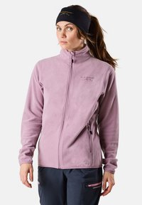 Vaaleanlila fleece-takki, jossa on korkea kaulus, täysi vetoketju ja sivutaskut. Pehmeä rakenne ja hillitty brändäys rinnassa.