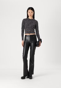 Zwarte neplederen flared pantalons met een hoge taille, gecombineerd met een aansluitend shirt met lange mouwen met een zwart-wit zilveren zebra print ontwerp.