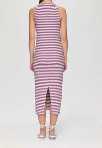 Femme portant une robe midi sans manches à rayures horizontales violettes et blanches avec une fente au dos, associée à des escarpins blancs à brides et talons kitten.