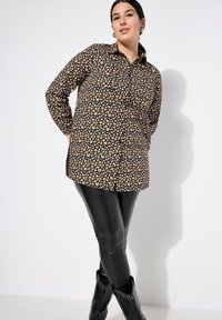 Zwarte shirt met een oranje hartpatroon, met knoopsluiting, lange mouwen en kraag. Gemaakt in combinatie met zwarte leggings en puntige laarzen.