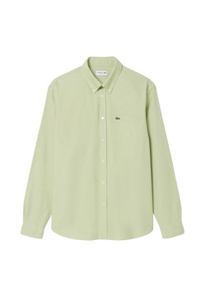 Camisa de manga larga verde claro con botones, bolsillo en el pecho y pequeño logo de cocodrilo Lacoste en el bolsillo, botones del cuello abrochados.