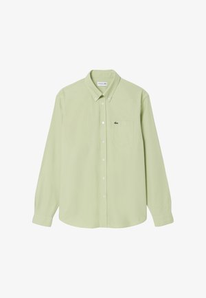 Camisa de manga larga verde claro con botones, bolsillo en el pecho y pequeño logo de cocodrilo Lacoste en el bolsillo, botones del cuello abrochados.