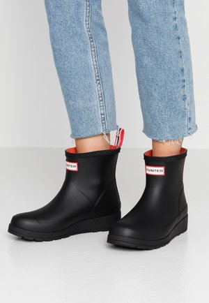 Ben iført korte lyseblå jeans og sorte Hunter-regnstøvler til anklerne med rødt indre og trækkeøjer.