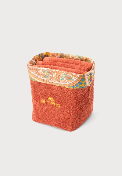 Serviette carrée pliée couleur rouille avec logo brodé et bordure en tissu à motif dans des tons orange, bleu et vert.