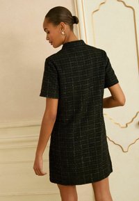 Czarna sukienka z krótkim rękawem o teksturowanym splocie, z kołnierzykiem i prostym krojem, z delikatnymi metalicznymi nitkami dodającymi całości charakteru.