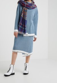 Blå ribbad stickad tröja och kjolset med vit randig trim, parat med en rutigt scarf. Modellen bär vita snörskor.