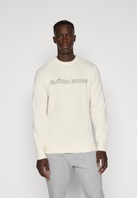 Cremfarbener Sweatshirt mit Rundhalsausschnitt und gerippten Bündchen, mit demtext "BJÖRN BORG" in fetten schwarzen Buchstaben über der Brust.