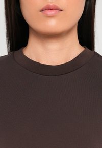 Sweatshirt en coton marron à col rond avec un encolure côtelée. Texture lisse, design ajusté, sans motifs ni ornements visibles.