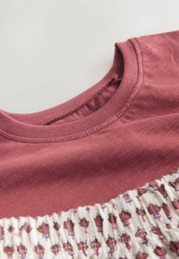 Nærbillede af en mørkerød crew neck-top kombineret med et hvidt smockstof med små mørkerøde blomsterprint.