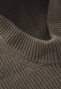 Gros plan sur un pull en tricot marron présentant une texture côtelée et un col haut. Le tissu semble doux et épais, soulignant la chaleur et le confort.