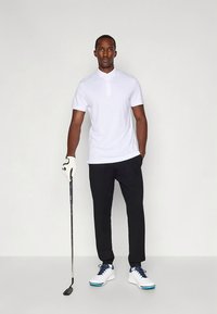 Balta polo krekls ar pogātu aizdari, melnas bikses un baltas kedas ar zilām detalizācijām. Tur golfu nūju un valkā cimdu.