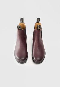 Botas de tobillo de cuero burdeos con paneles laterales elásticos y lengüetas para tirar. Suelas de goma negra resistentes para mayor tracción. Acabado liso con costuras mínimas.