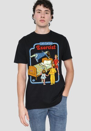 Man wearing black T-shirt with colorful vintage-style graphic of a levitating girl above a bed and three children watching, text "Let's Call the Exorcist."
