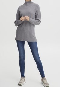 Maglione grigio a maglia con colletto alto, vestibilità rilassata, polsini e orlo a coste, abbinato a jeans skinny blu e sneakers grigio chiaro.