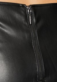 Prenda de cuero negro con un primer plano de una cremallera plateada. El material tiene una textura suave y la cremallera va en vertical a lo largo del centro.