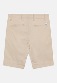 Shorts en coton beige avec une texture lisse, dotés de deux poches arrière zippées et de passants de ceinture, bords ourlés, et d'une petite étiquette de marque.
