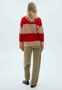 Röd och beiga randig tröja med lös passform, kompletterad med olivgröna vida byxor och svarta skor, sedd bakifrån.