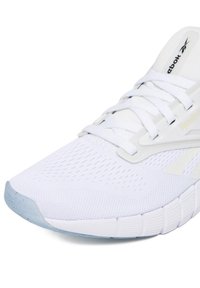 Biela športová obuv s sieťovaným zvrškom, zaväzovaním na šnúrky a svetlomodrou gumovou podrážkou. Má branding Reebok a textúrované detaily.