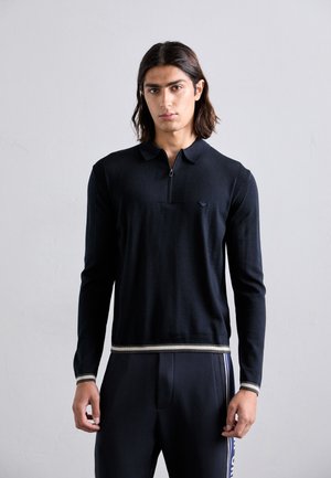 Marineblauwe polo met lange mouwen en een ritskraag, ribbelstructuur en contrasterende gestreepte zoom. Heeft een klein logo op de borst.