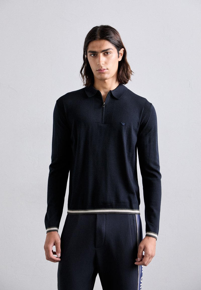 Polo shirt cu mâneci lungi de culoare bleumarin, cu guler cu fermoar, textură ribbed și margine cu dungi contrastante. Prezintă un logo mic pe piept.