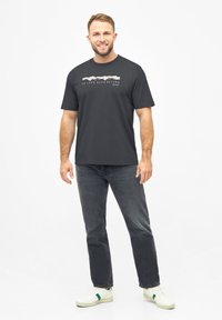Donkergrijze t-shirt met korte mouwen en een grafische tekstprint "VERLIEFD OP DE NATUUR" op de voorkant. Draagt het met donkere jeans en witte sneakers.