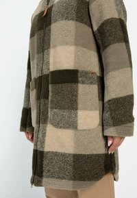 Karierten Mantel aus weichem, dickem Stoff mit beige-grünen Quadraten, einem Frontreißverschluss, zwei Seitentaschen und einem leicht geschwungenen Saum.