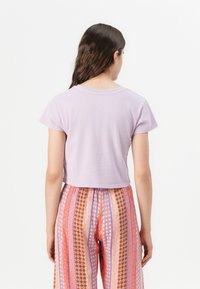 Lühike lavendli värvi crop top lühikeste varrukatega, koos mustriliste, mitmevärviliste laia säärega pükstega, millel on triibud ja lillemotiivid.