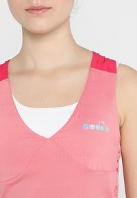 Rosa träningslinne med strukturtyg, V-ringning och kontrasterande rosa axeldetaljer. Har ett präglat logotyp på bröstet.