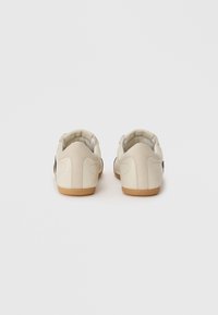 Baskets en cuir blanc avec semelles en caoutchouc beige. Forme arrondie, design minimaliste, avec des accents cousus et une finition lisse.