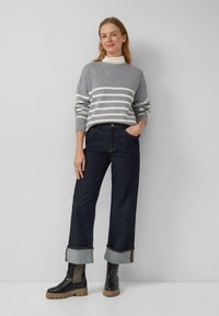 Grau gestreifter Pullover mit hohem Kragen, dunkle weit geschnittene Jeans mit umgeschlagenen Säumen und schwarze Knöchelstiefel mit robusten Sohlen.