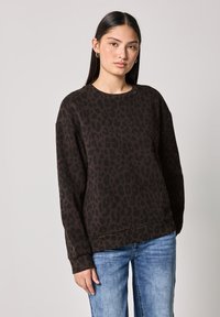 Sweatshirt marron avec imprimé léopard noir, encolure ronde, manches longues et poignets côtelés, associé à un jean bleu. Texture douce.