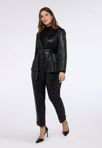 Černá umělá kožená sako s páskem na zavázání, v kombinaci se shodnými zúženými kalhotami a černými špičatými lodičkami. Hladká textura, přizpůsobený střih.