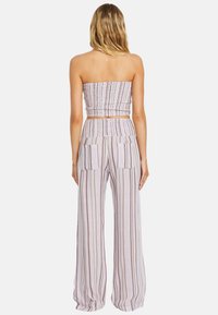 Dwuczęściowy strój w paski, składający się z górnej części bez ramiączek z marszczeniem oraz wysokich spodni o szerokich nogawkach z przednimi kieszeniami w jasnych odcieniach.