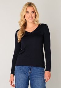 Navyblauw shirt met lange mouwen en een V-hals, gemaakt van zachte stof, gecombineerd met lichtblauwe spijkerbroek. Gladde textuur, eenvoudige silhouet.