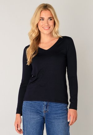 Navyblauw shirt met lange mouwen en een V-hals, gemaakt van zachte stof, gecombineerd met lichtblauwe spijkerbroek. Gladde textuur, eenvoudige silhouet.