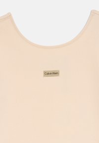 Camiseta bege da Calvin Klein com decote redondo e um pequeno emblema retangular no centro, feita de um tecido liso e suave.