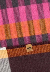 Mehrfarbiges Karomuster-Decke mit pinken, orangefarbenen und grauen Mustern sowie einer strukturierten Oberfläche. Ein kleines Stoffetikett ist am Rand angebracht.
