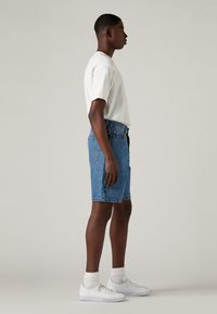 Blå denimshorts, kuttet over kneet, kombinert med en hvit T-skjorte med rund hals og hvite joggesko med ankelsokker.