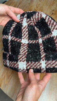 Kötött sapka fekete, fehér és bordó kockás mintával; texturált, bolyhos hatású anyag; feltekerhető szegély; arany színű díszítések.