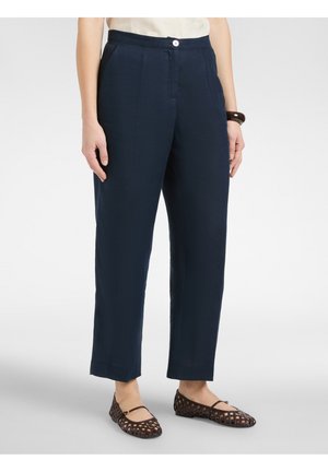 Mujer con pantalones azules marino de pierna recta y corte cropped, top crema, bailarinas oscuras tejidas y una pulsera oscura en su muñeca derecha.