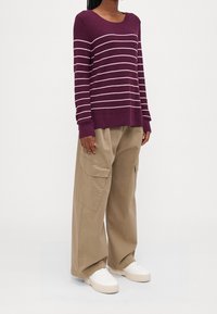 Lila randig tröja med vita linjer, stickad struktur; kombinerad med lösa, khaki cargobyxor och vita sneakers. Enkla, moderna designelement.