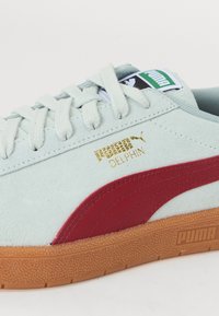 Tenisky PUMA Delphin s lehkým zeleným semišem, červeným koženým pruhem, gumovou podrážkou a zlatými logovými akcenty.