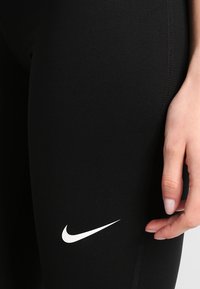 Nike svarta leggings med en slät yta, åtsittande design och en framträdande vit Swoosh-logga på vänster lår.