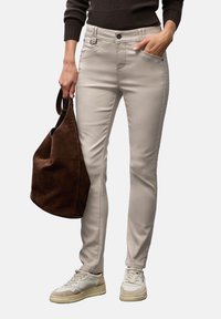 Světlé béžové slim-fit kalhoty s knoflíkovým zapínáním a předními kapsami, doplněné hnědým semišovým tote bagem a bílými teniskami.