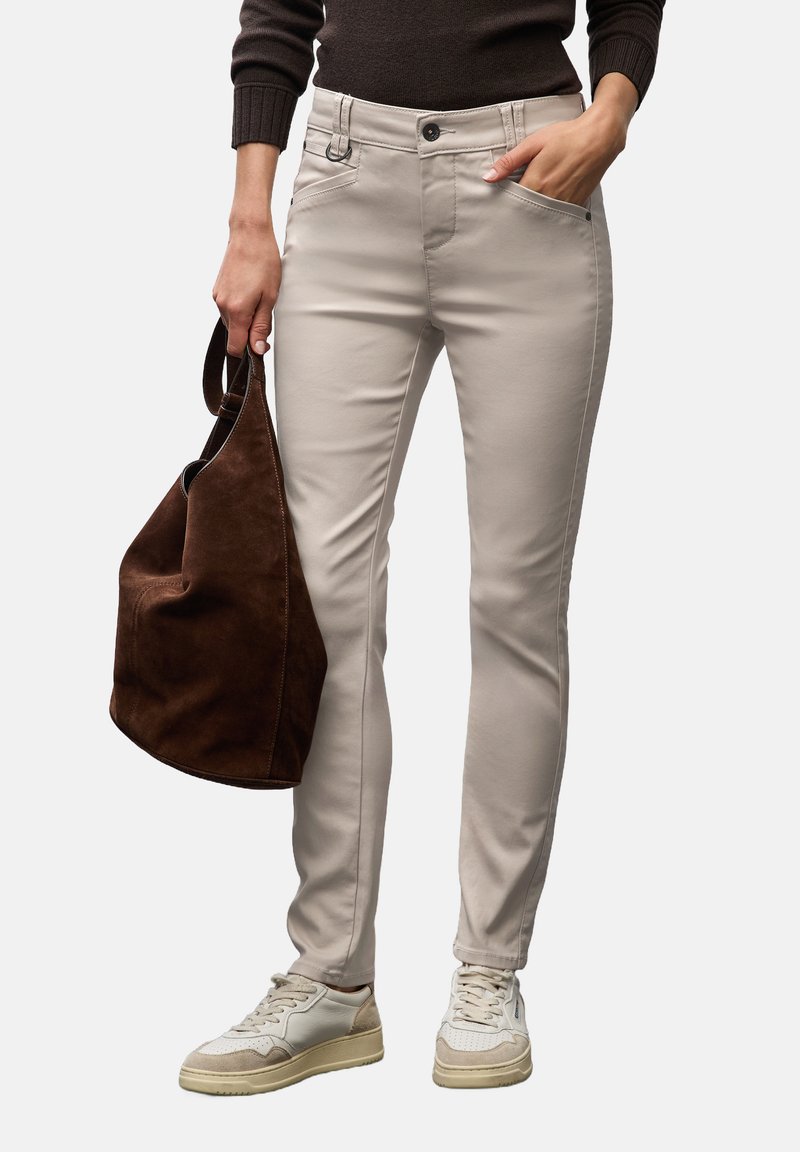 Světlé béžové slim-fit kalhoty s knoflíkovým zapínáním a předními kapsami, doplněné hnědým semišovým tote bagem a bílými teniskami.