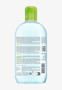 Bouteille en plastique transparent avec un bouchon à bascule vert, contenant de l'eau micellaire. L'étiquette comporte un texte multilingue détaillant les instructions d'utilisation et les ingrédients.