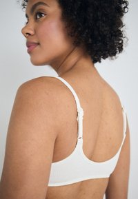 White textured bra with adjustable straps featuring a looped accent. Smooth fabric and a simple design emphasize minimalism.